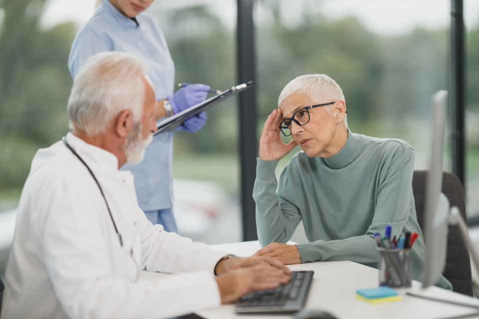 A physician, a patient and a clinical staff member meeting at a desk in a medical practice office.